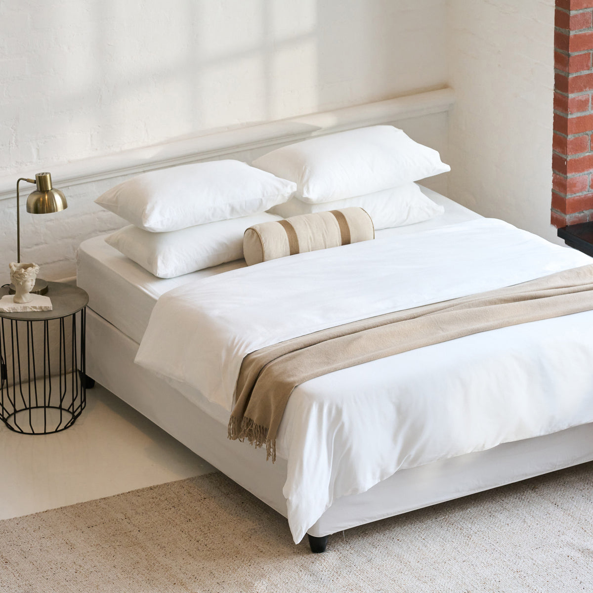 White Himmel duvet cover set styled with a beige throw and bolster cushion on a bed with a brick fireplace and brass lamp