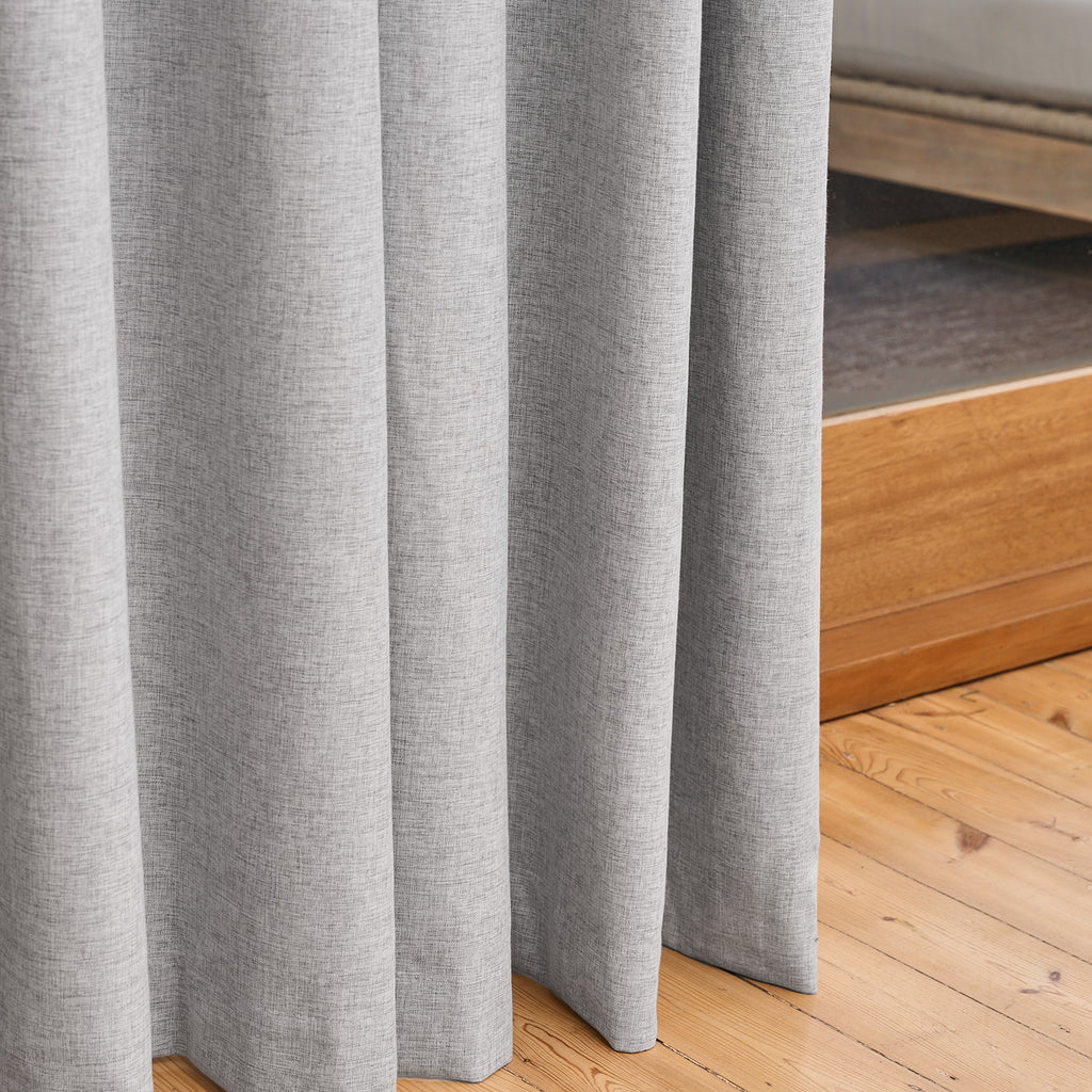 Close-up of the Sinclair curtain's hem pooling on a wooden floor in creme grey