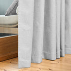 Close-up of the Dakota curtain's hem pooling on a wooden floor in pearl grey, beside a daybed